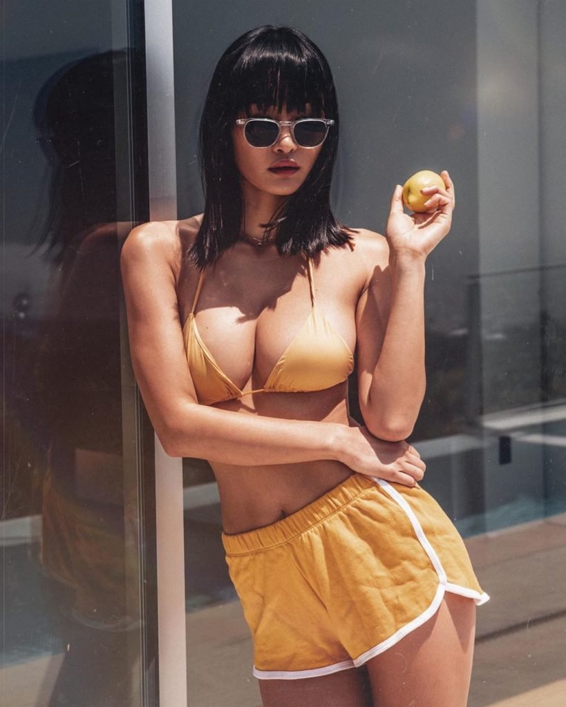 Miki Hamano Modelo Oriental de look amarelo óculos e uma fruta na mão