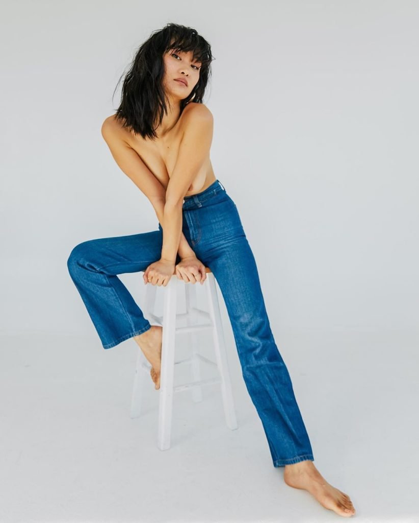 Miki Hamano Modelo Oriental de calça jeans sentada na cadeira seminua