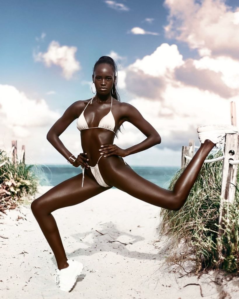 Quiyona Modelo Negra em pose conceitual na praia de biquíni branco e tênis branco