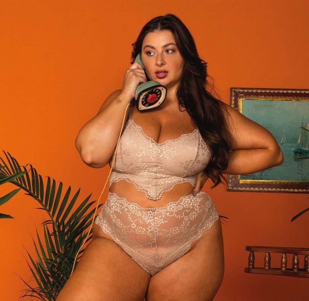 Letticia Munniz Modelo Plus Size posando de lingerie rosa falando ao telefone