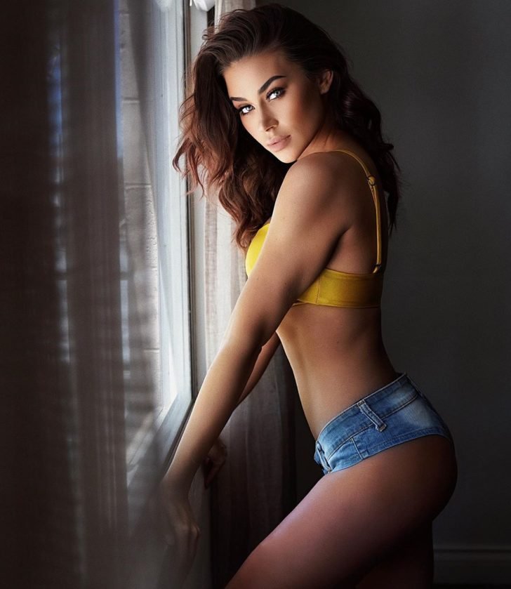 Masha Modelo Morena de shorts jeans blusinha amarela apoiada na janela