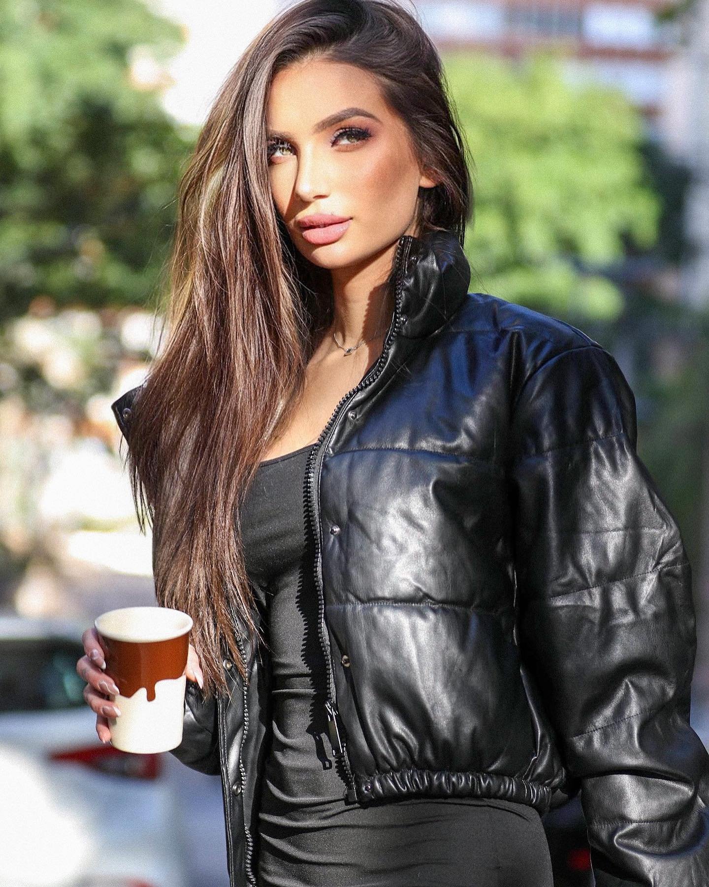 Stefani Bays Influencer posando de look preto e jaqueta copo na mão