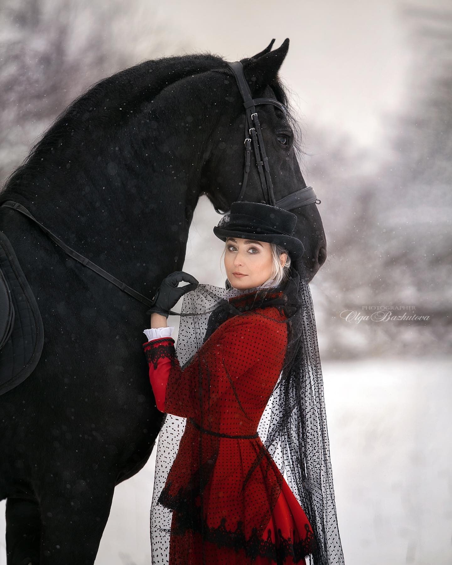 Olga Bazhutova fotografia equestre - Modelo em figurino vermelho posando com cavalo preto na neve